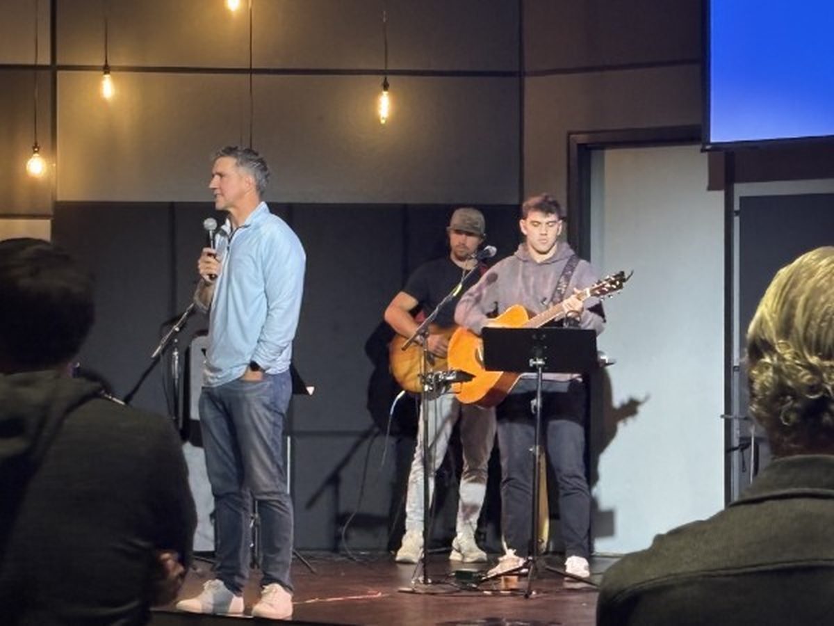 A speaker on stage with worship musicians during a 12 Tribes night